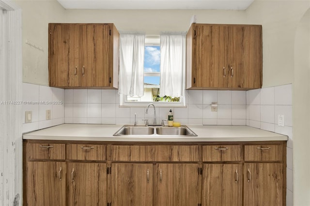 kitchen with decorative backsplash, brown cabinetry, light countertops, and a sink