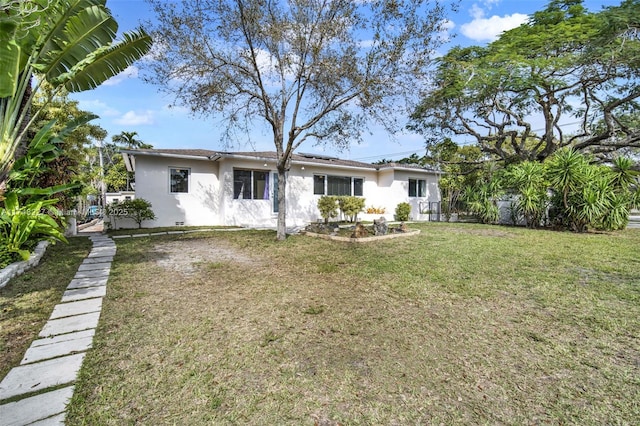 rear view of property featuring fence, a lawn, and stucco siding