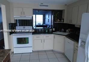 kitchen featuring white cabinetry, a sink, light tile patterned flooring, white appliances, and under cabinet range hood