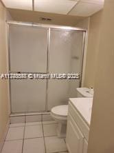 bathroom with a paneled ceiling, toilet, a shower with shower door, vanity, and tile patterned floors