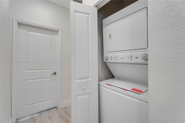 laundry room featuring stacked washer and dryer, light wood-type flooring, laundry area, and a textured wall