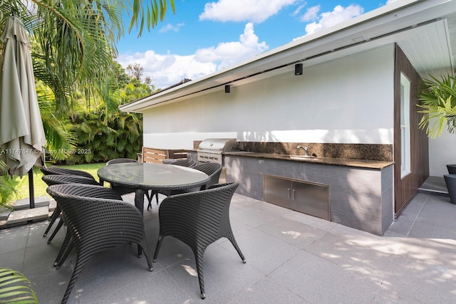 view of patio with area for grilling, a grill, outdoor dining space, and a sink