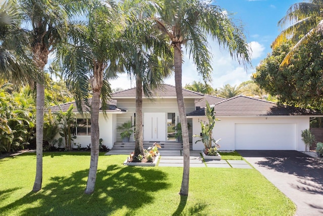 view of front facade featuring aphalt driveway, a tile roof, a front yard, stucco siding, and a garage