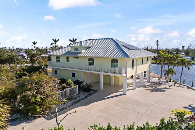 exterior space featuring driveway, metal roof, a water view, a standing seam roof, and roof mounted solar panels