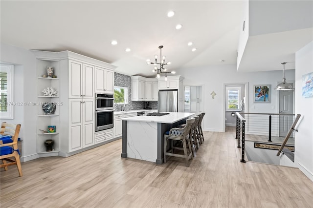 kitchen with a center island, hanging light fixtures, appliances with stainless steel finishes, white cabinetry, and a kitchen breakfast bar