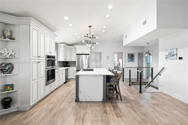 kitchen featuring white cabinets, decorative light fixtures, a center island, stainless steel appliances, and a kitchen bar