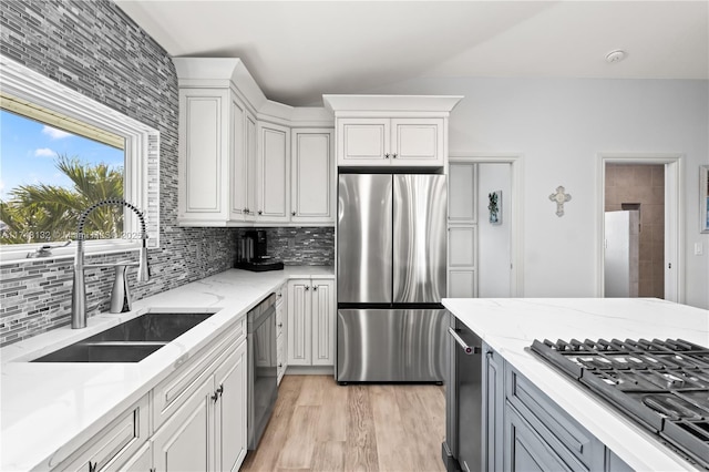 kitchen with appliances with stainless steel finishes, white cabinets, a sink, and light stone counters