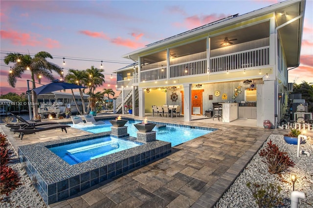 pool at dusk with a patio, an outdoor kitchen, ceiling fan, an outdoor bar, and stairs