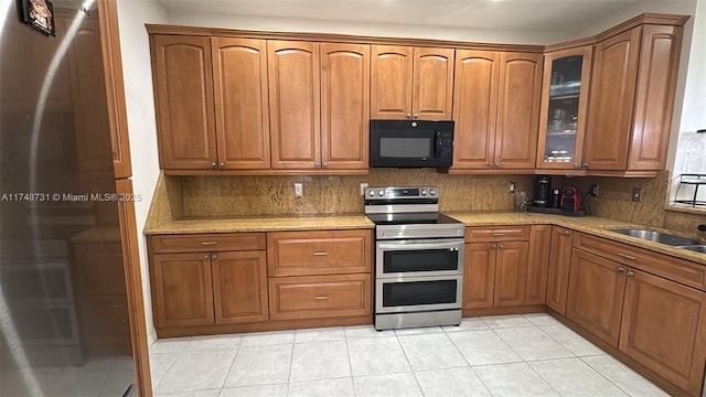 kitchen featuring stainless steel appliances, brown cabinets, glass insert cabinets, and decorative backsplash