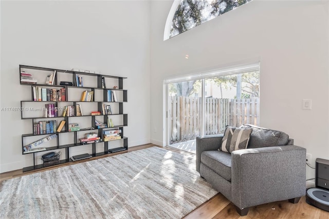 sitting room with baseboards, a towering ceiling, wood finished floors, and a healthy amount of sunlight