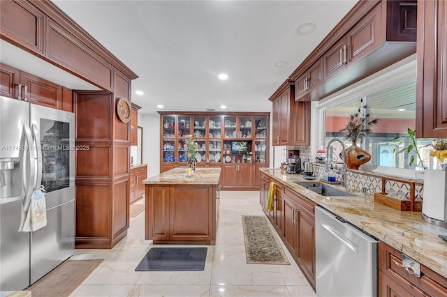 kitchen featuring appliances with stainless steel finishes, light stone countertops, a sink, and a kitchen island