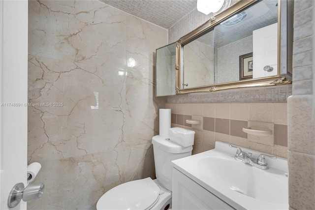 bathroom featuring toilet, tile walls, and vanity