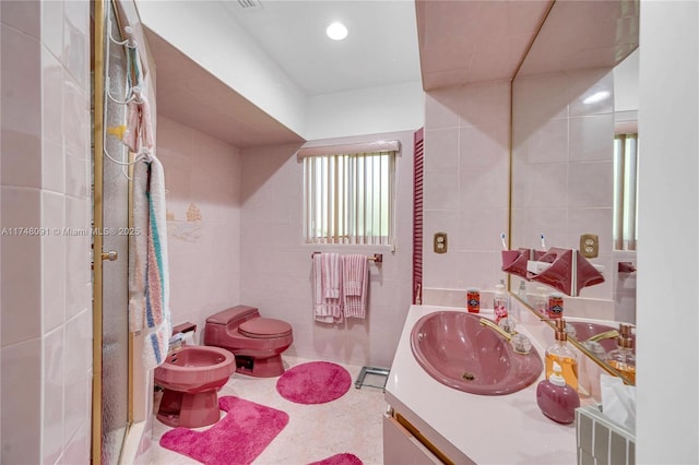 bathroom featuring toilet, a bidet, vanity, and tile walls