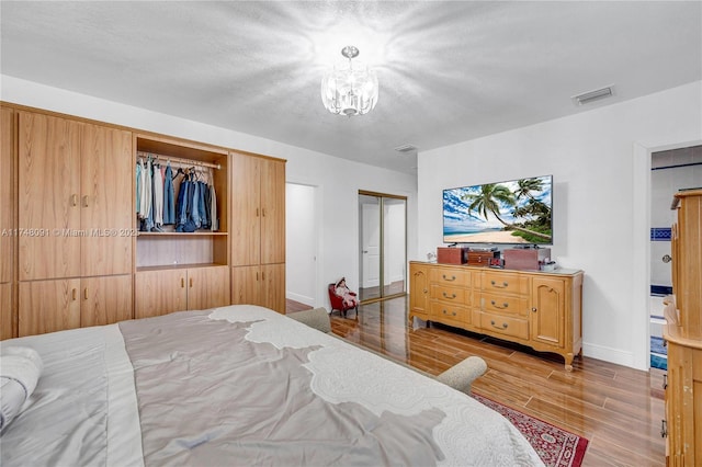 bedroom featuring light wood finished floors, baseboards, visible vents, a textured ceiling, and a notable chandelier