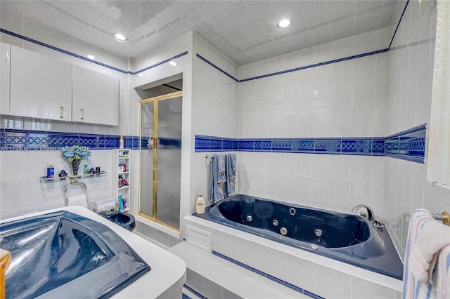 bathroom with a stall shower, tile walls, and a tub with jets