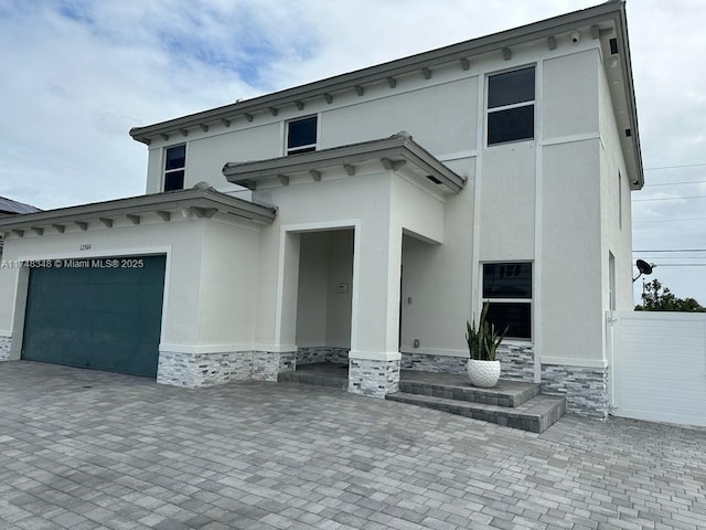 italianate house with decorative driveway, stone siding, a garage, and stucco siding