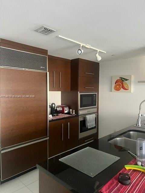 kitchen featuring dark countertops, visible vents, light tile patterned flooring, a sink, and built in appliances