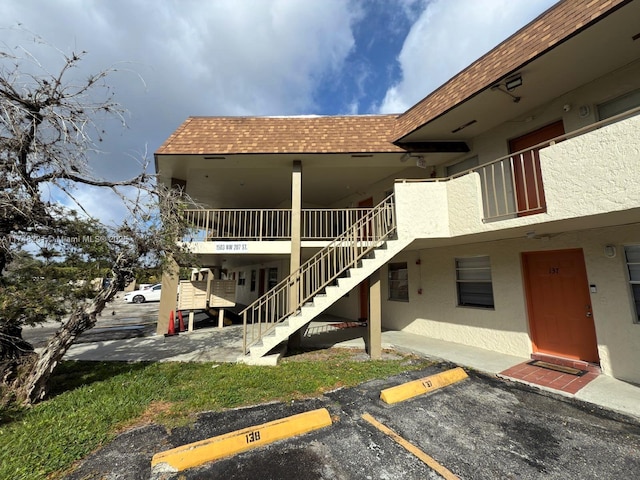 exterior space with stairway, roof with shingles, a patio area, uncovered parking, and stucco siding