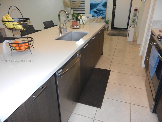 kitchen featuring light tile patterned floors, dishwashing machine, a sink, light countertops, and dark brown cabinets