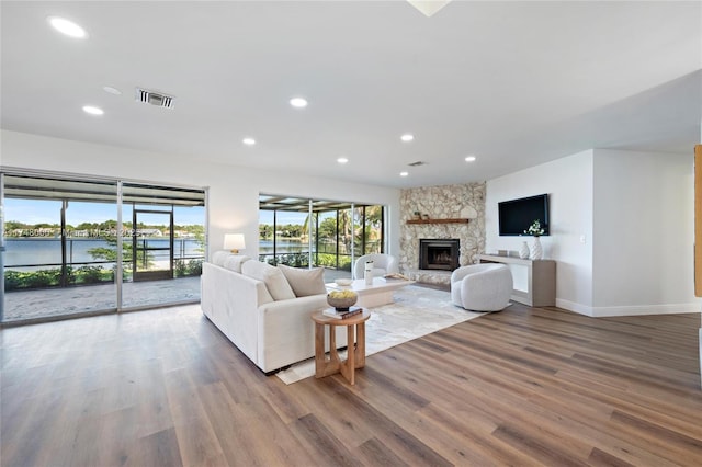 living room featuring recessed lighting, wood finished floors, visible vents, a fireplace, and a water view