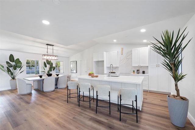 kitchen featuring light wood-style flooring, hanging light fixtures, white cabinetry, light countertops, and a center island with sink