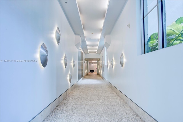 hallway featuring light speckled floor and baseboards