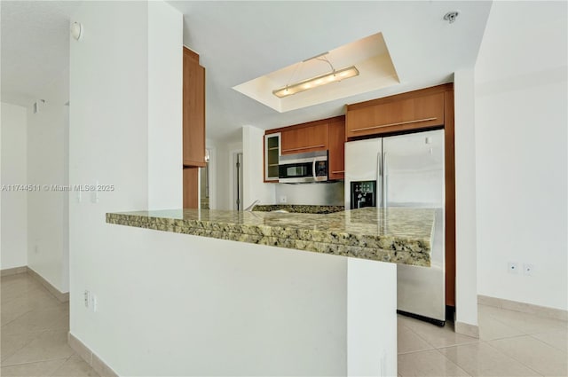 kitchen with a peninsula, light stone countertops, stainless steel appliances, and brown cabinetry