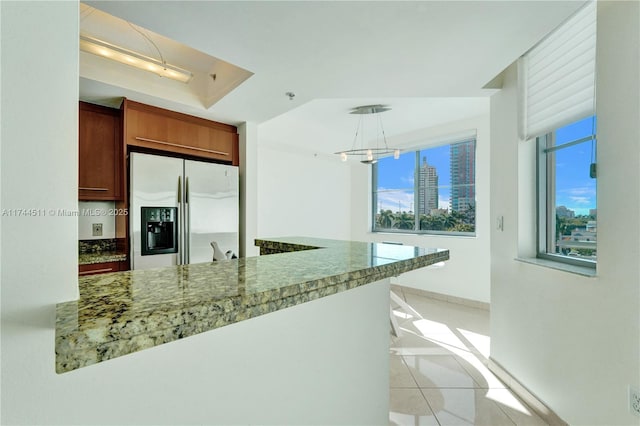 kitchen with stainless steel fridge with ice dispenser, brown cabinets, dark stone countertops, decorative light fixtures, and light tile patterned flooring