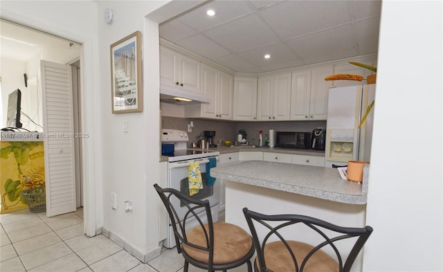 kitchen with white appliances, under cabinet range hood, white cabinetry, and a drop ceiling