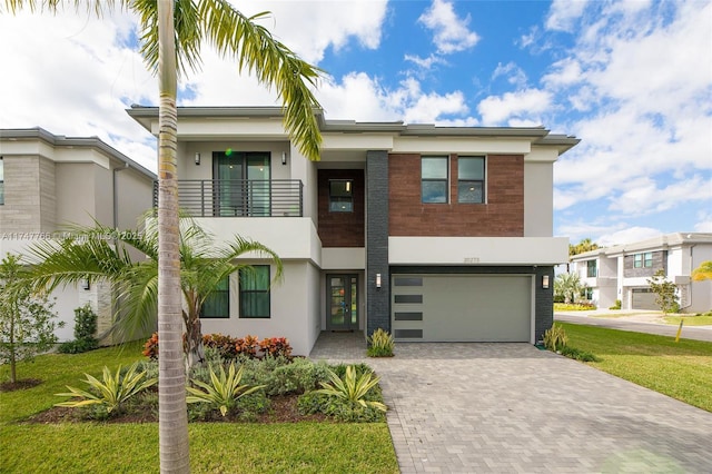 view of front of home with decorative driveway, an attached garage, a balcony, and stucco siding