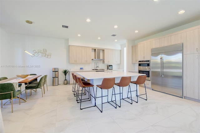 kitchen with light countertops, visible vents, light brown cabinetry, appliances with stainless steel finishes, and wall chimney exhaust hood