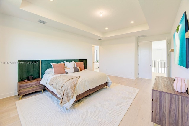 bedroom with light wood-style floors, a tray ceiling, visible vents, and baseboards