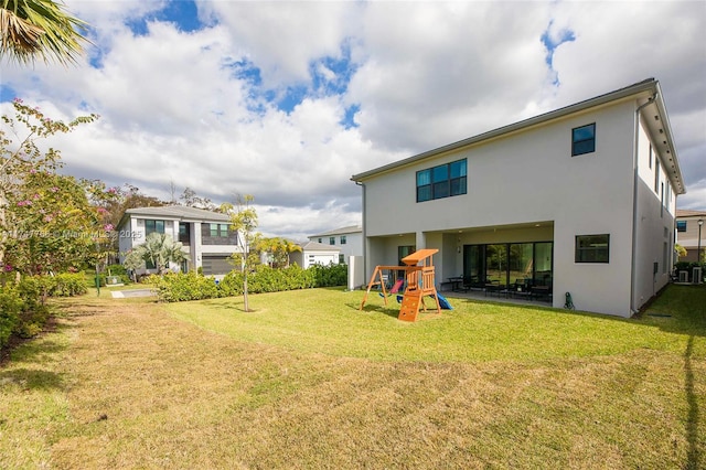 back of property featuring a lawn, a playground, and stucco siding