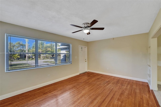 empty room with a ceiling fan, light wood-type flooring, a textured ceiling, and baseboards