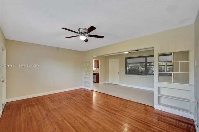 interior space with baseboards, a textured ceiling, a ceiling fan, and wood finished floors