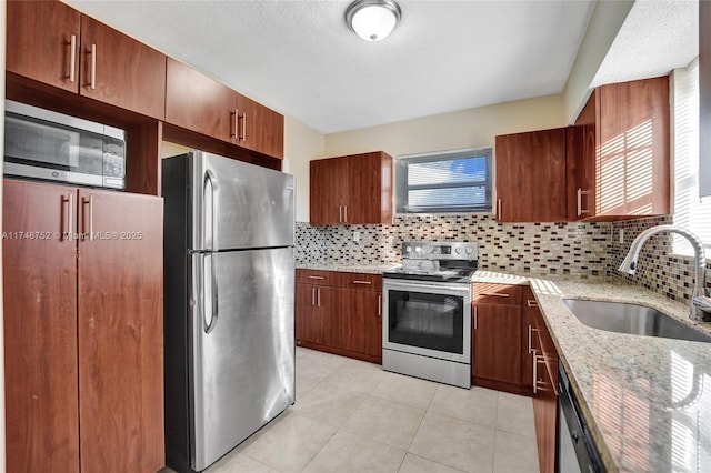 kitchen featuring light stone counters, tasteful backsplash, appliances with stainless steel finishes, light tile patterned flooring, and a sink