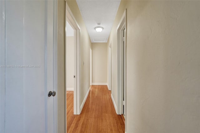 hallway featuring baseboards, a textured ceiling, and light wood-style floors