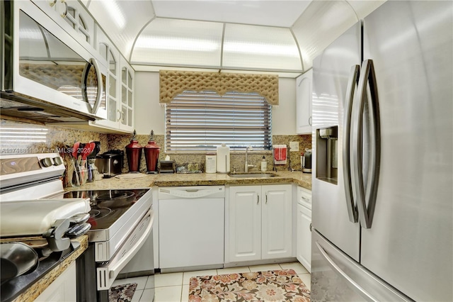 kitchen with light tile patterned floors, glass insert cabinets, appliances with stainless steel finishes, white cabinetry, and a sink