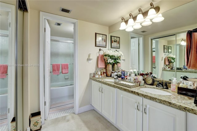 bathroom featuring shower / bath combination with glass door, visible vents, a sink, and double vanity