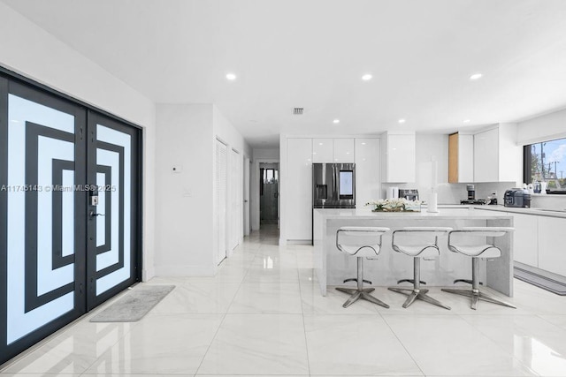 kitchen featuring french doors, light countertops, white cabinetry, stainless steel fridge, and a kitchen bar