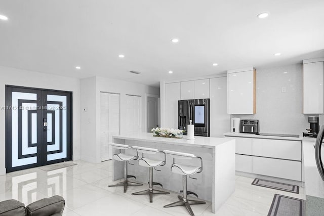 kitchen with a breakfast bar area, white cabinetry, stainless steel fridge with ice dispenser, a center island, and modern cabinets