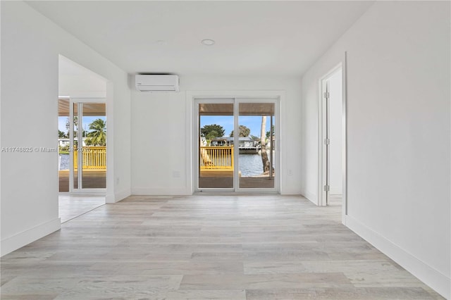 empty room with light wood-type flooring, a healthy amount of sunlight, a water view, and a wall mounted AC