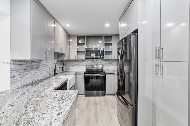 kitchen with light stone counters, a sink, appliances with stainless steel finishes, decorative backsplash, and modern cabinets