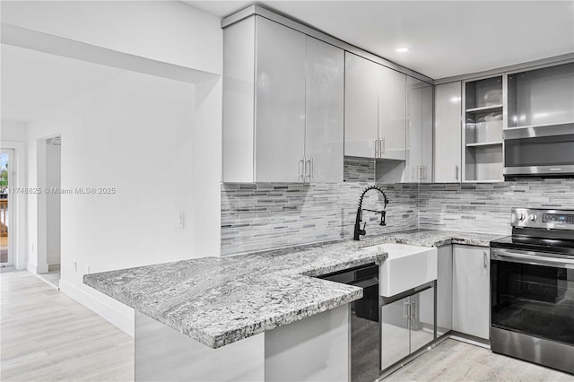 kitchen featuring light wood finished floors, appliances with stainless steel finishes, glass insert cabinets, light stone countertops, and a peninsula