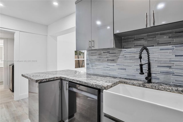 kitchen with stone countertops, decorative backsplash, a peninsula, gray cabinetry, and a sink