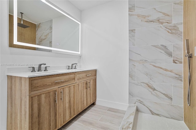 full bath featuring double vanity, walk in shower, a sink, and baseboards