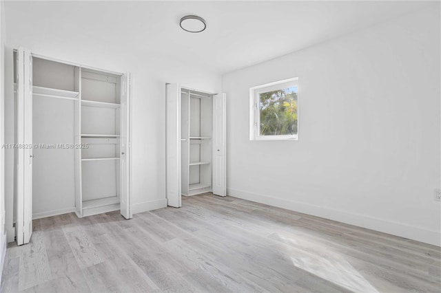 unfurnished bedroom featuring light wood-type flooring, baseboards, and multiple closets