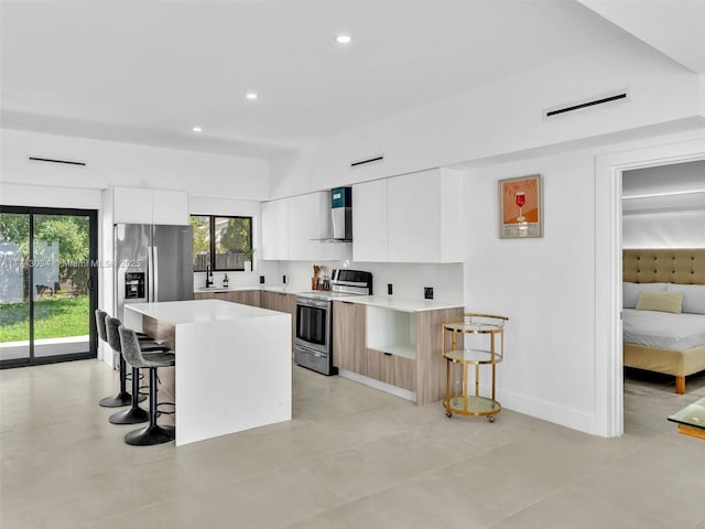 kitchen featuring wall chimney range hood, a sink, stainless steel appliances, a kitchen breakfast bar, and modern cabinets