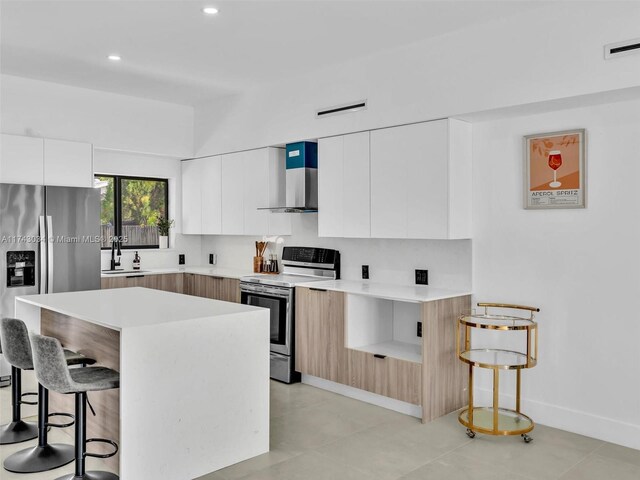 kitchen featuring visible vents, appliances with stainless steel finishes, a kitchen bar, wall chimney exhaust hood, and modern cabinets