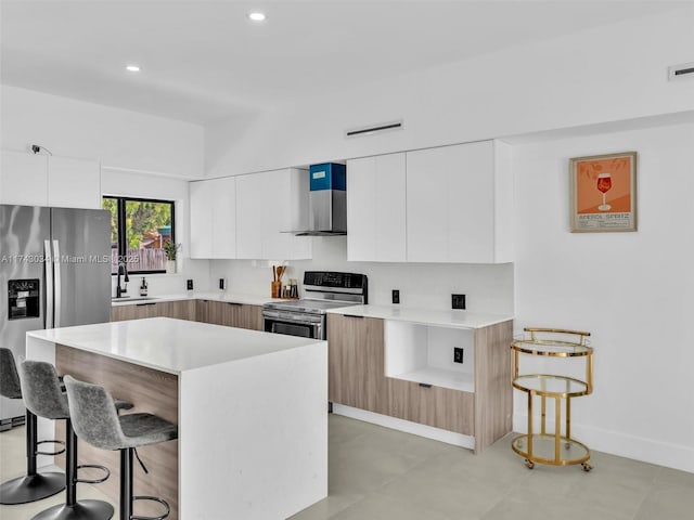 kitchen with a breakfast bar, a sink, appliances with stainless steel finishes, wall chimney range hood, and modern cabinets